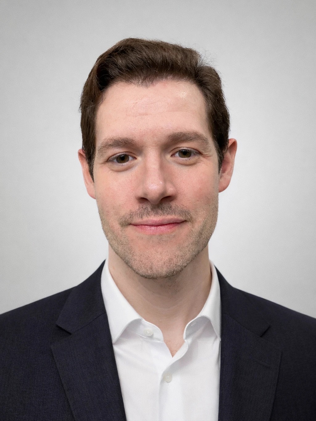 David Walker, photographed in a studio against a plain grey background, in a navy suit jacket over an open white shirt.