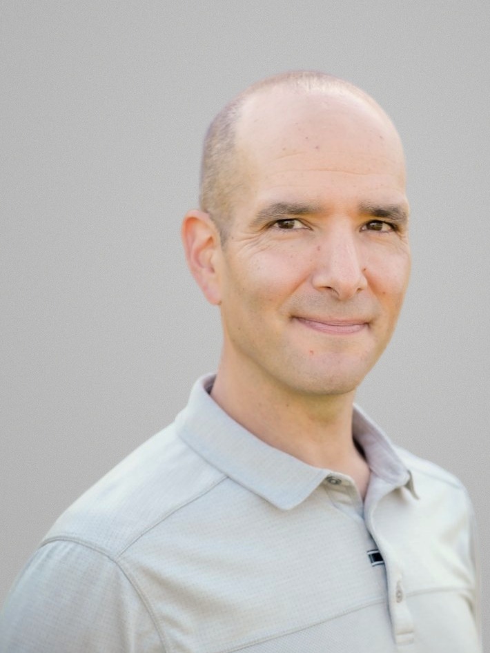 Matthew Pearlson, photographed in a studio against a plain grey background, in a pale grey polo shirt, turned slightly to camera.
